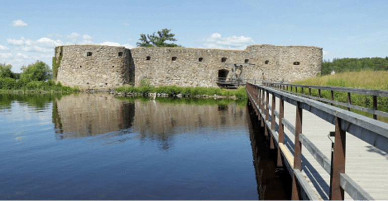 Gångbro över vattendrag med Kronobergs fästning i bakgrunden.